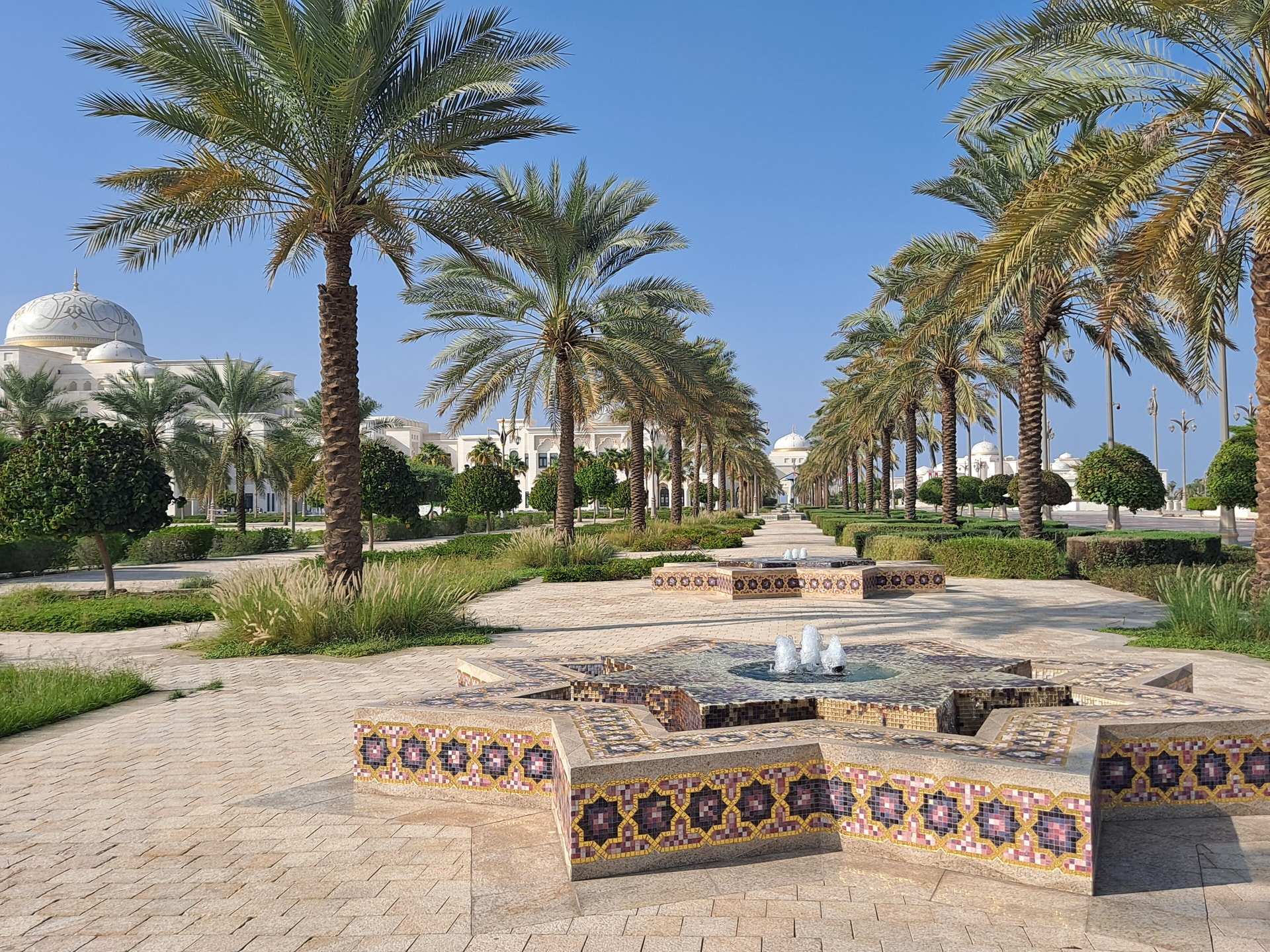 A tiled, star-shaped fountain on a palm-lined avenue in the grounds of Qasr Al Watan, Abu Dhabi, with the palace's white domes behind