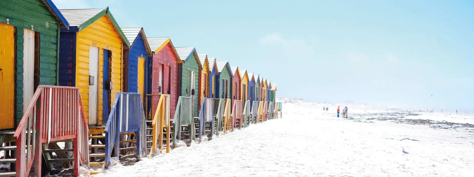 A row of brightly painted beach huts on white sand
