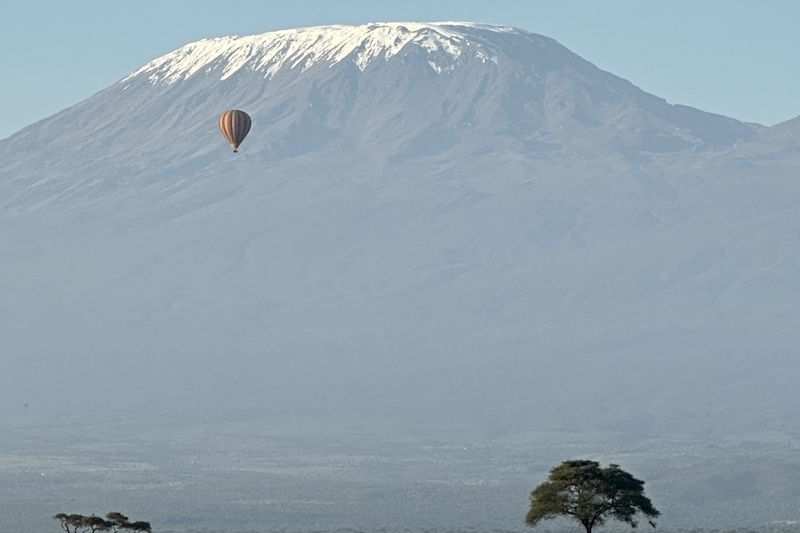A hot-air balloon drifting below the snows of Kilimanjaro, above Amboseli's grassland