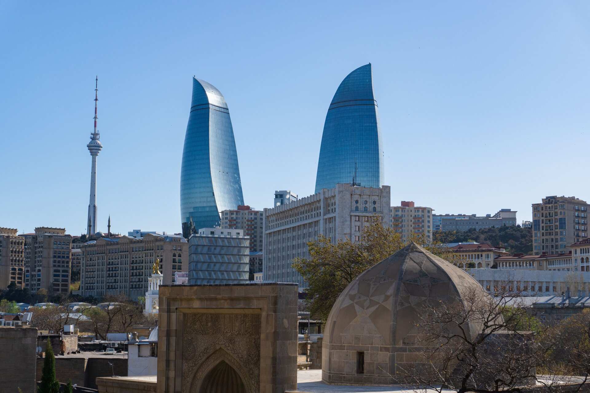 The Flame Towers rising behind the domed stone roofs and carved portal of Baku's walled old city under a clear sky