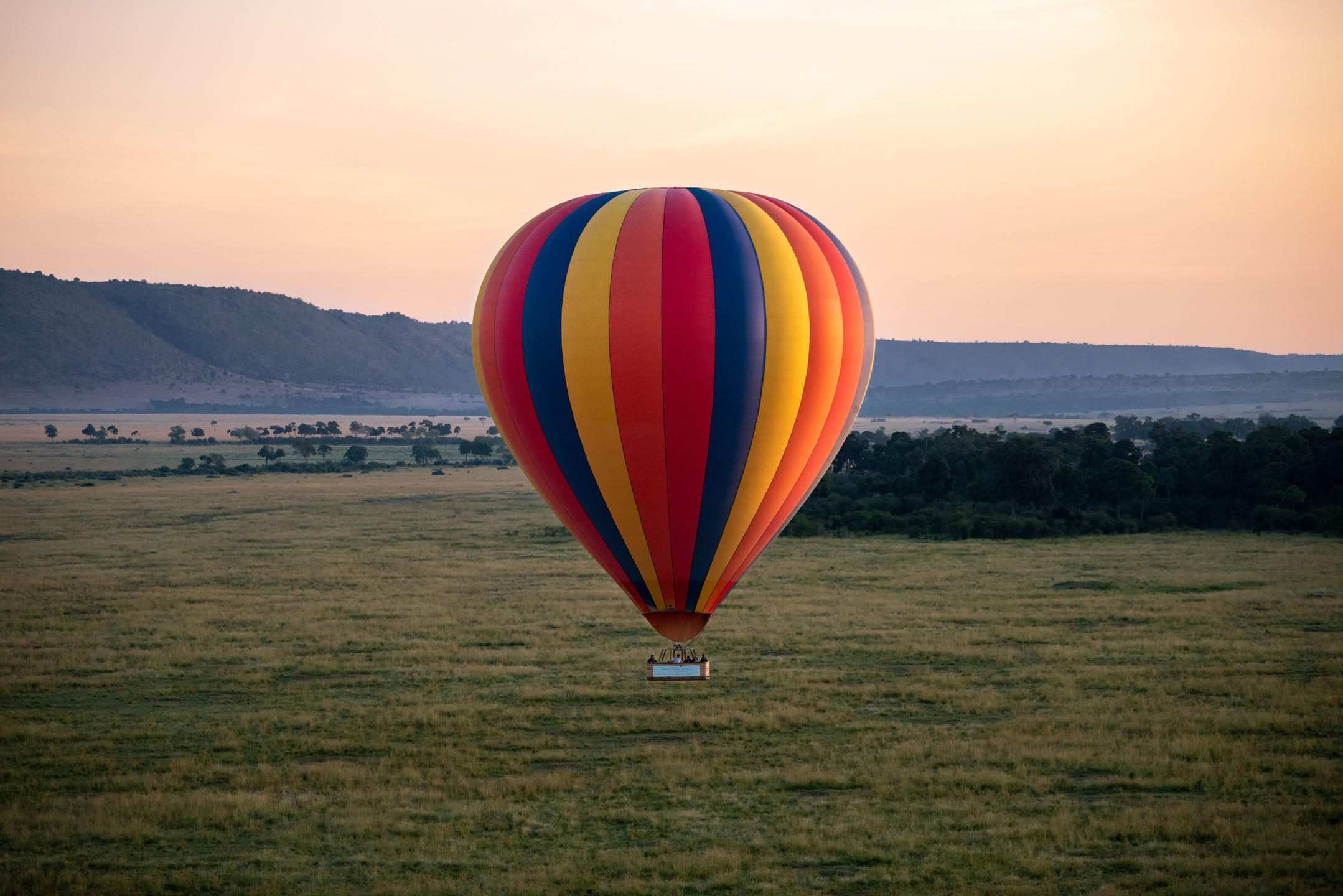 Two hot-air balloons standing inflated and lit at dawn on a clearing beside a camp, seen from above