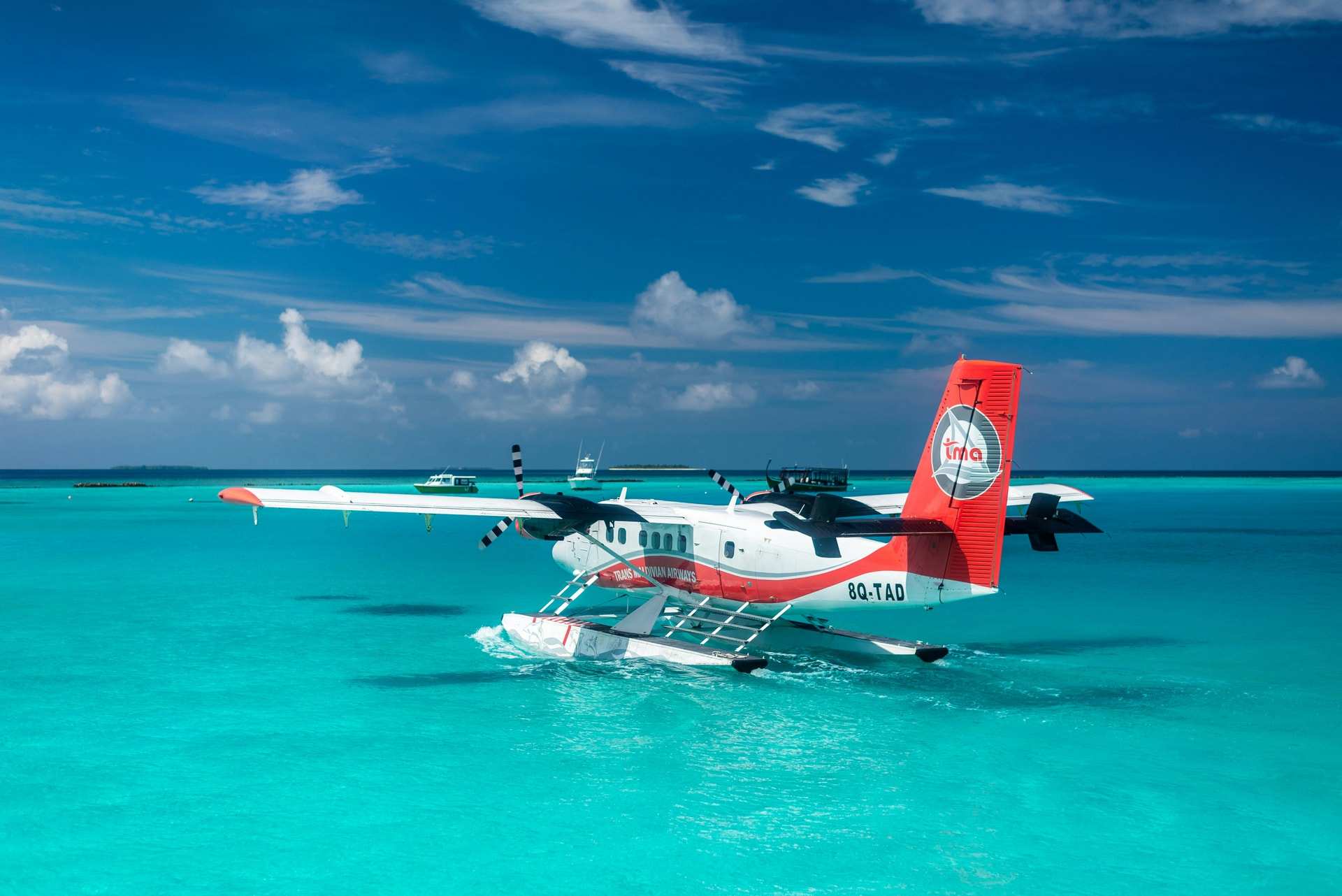 A red and white seaplane on floats in a bright turquoise lagoon under a blue sky with small clouds
