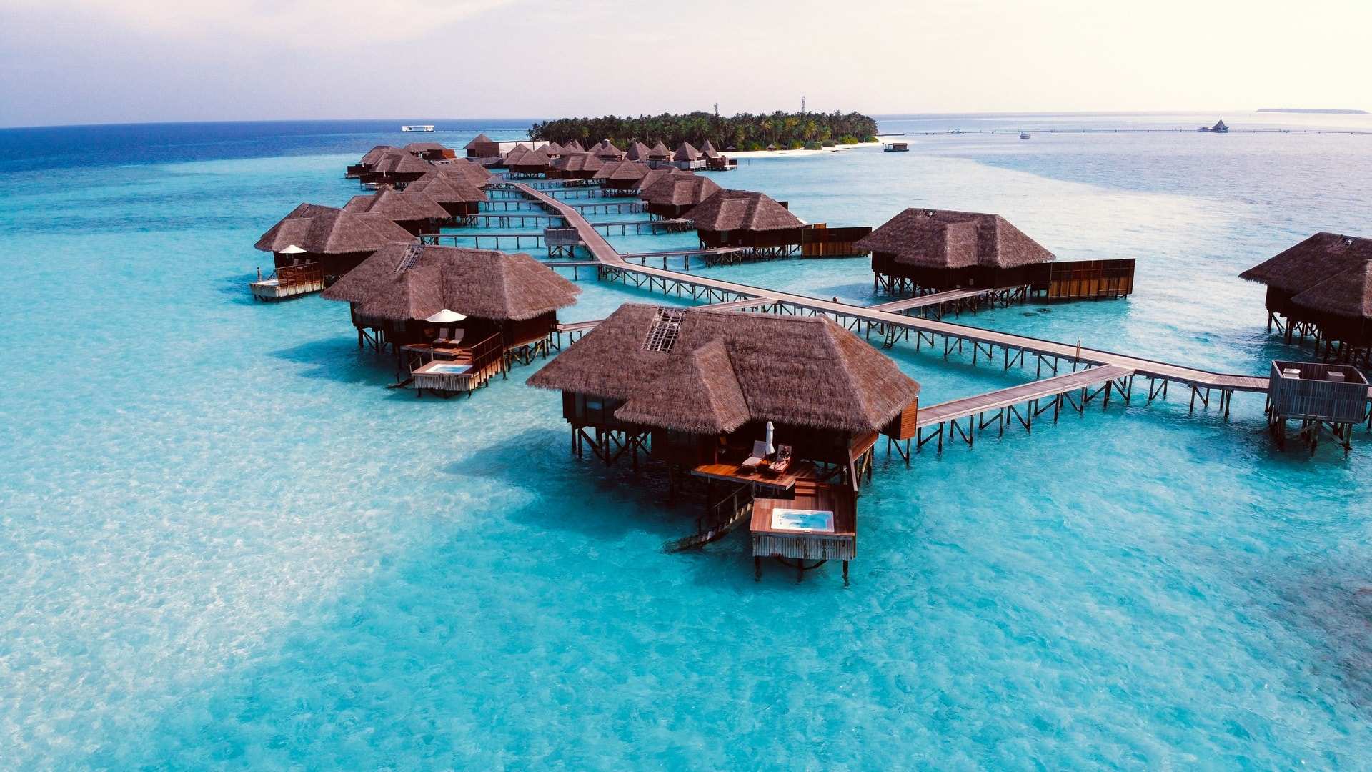 Overwater villas with thatched roofs on a curving wooden jetty above a clear turquoise lagoon in the Maldives