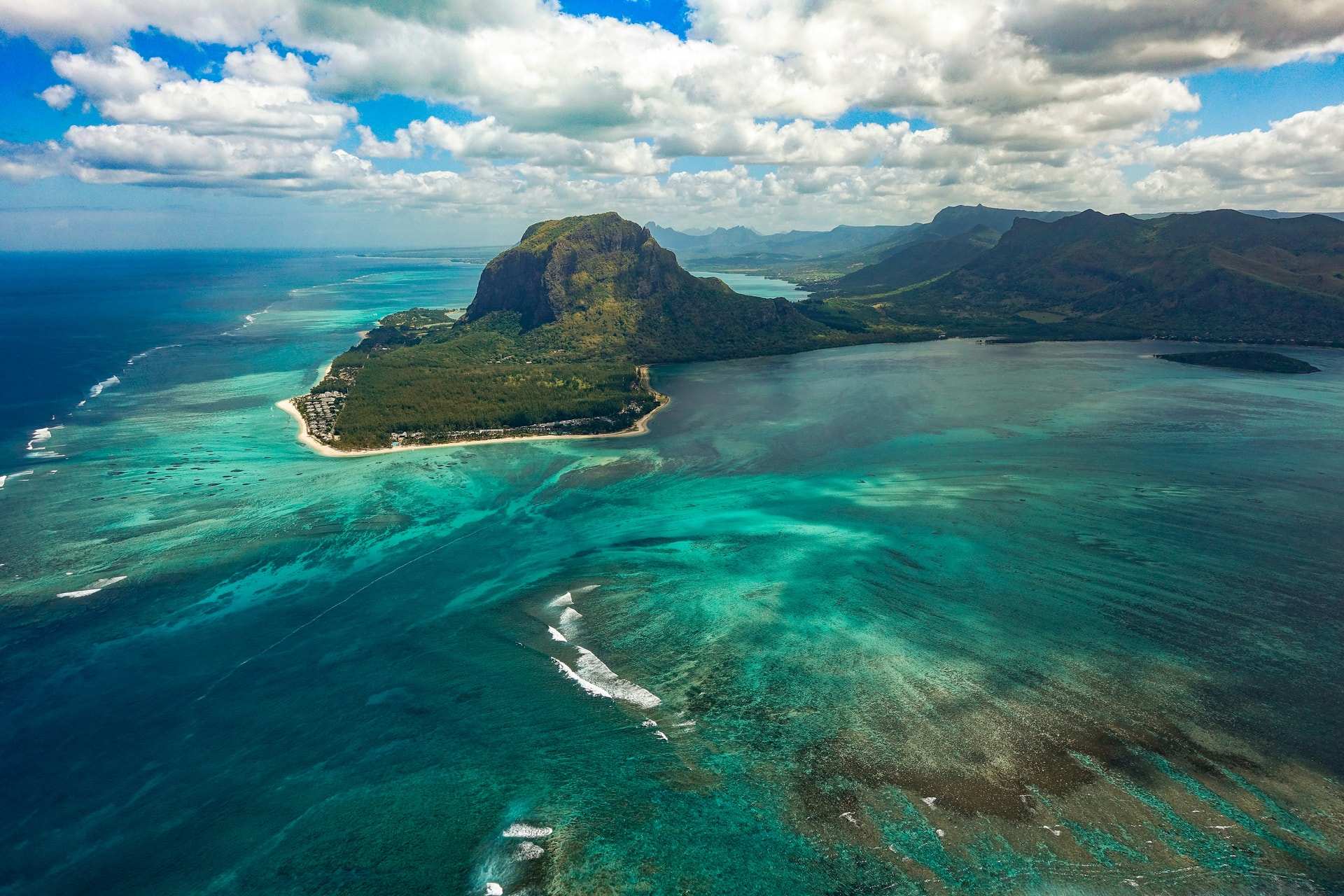 Aerial view of the Le Morne peninsula in south-west Mauritius, its mountain above a wide turquoise lagoon and the reef edge beyond
