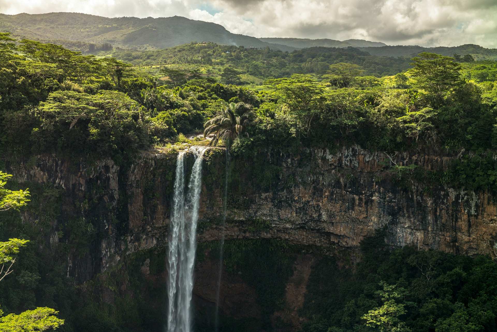 A tall, thin waterfall dropping into a forested gorge in the green interior of Mauritius