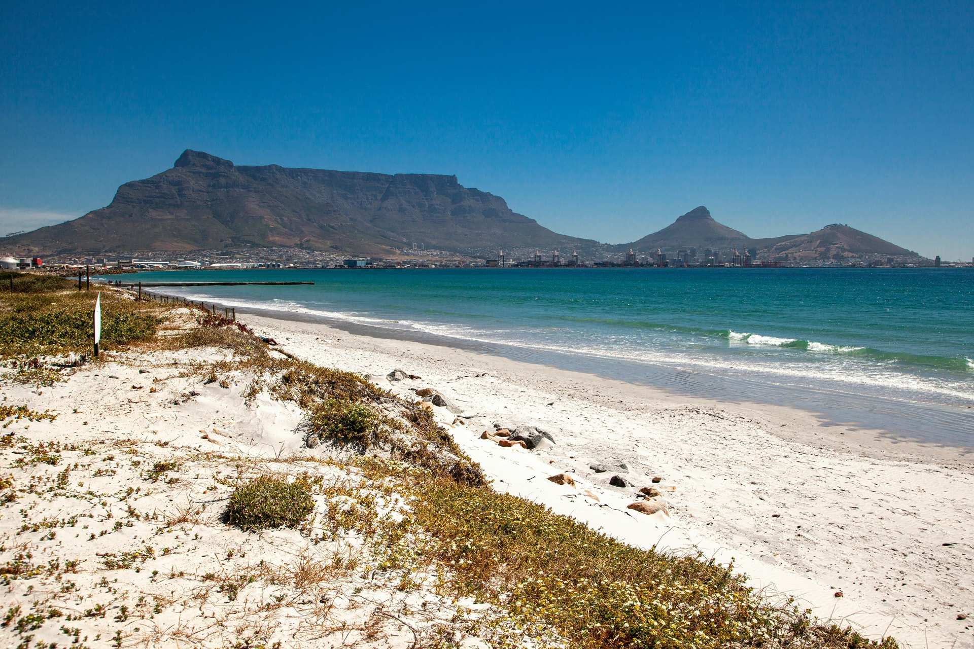 Table Mountain across the bay from a white beach at Milnerton, Cape Town, under a clear blue sky