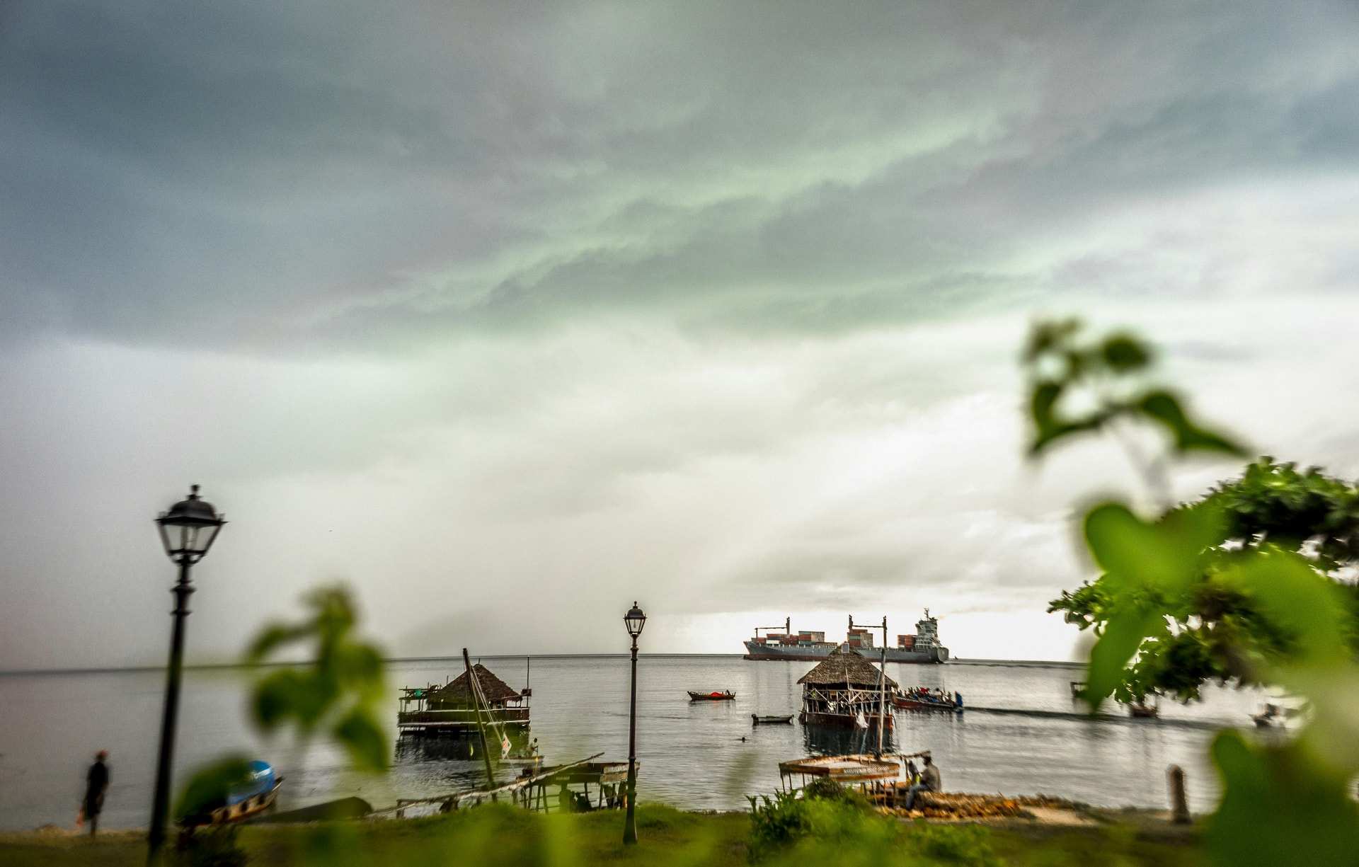 Heavy grey rain clouds over the Stone Town waterfront, boats moored offshore and a street lamp in the foreground