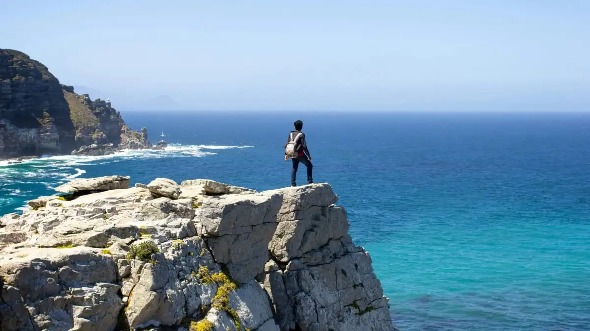 A traveller standing on a cliff edge above turquoise water