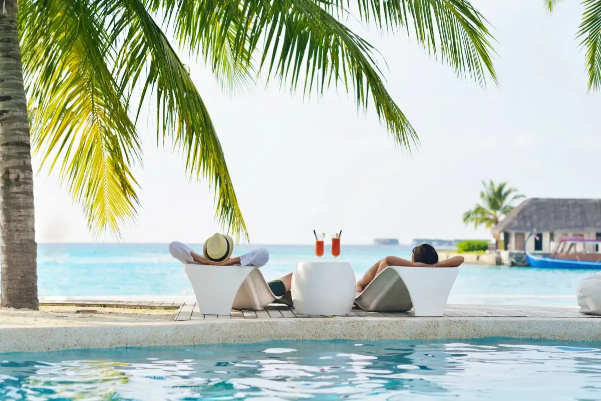 Two people relaxing in a pool with drinks, under palms