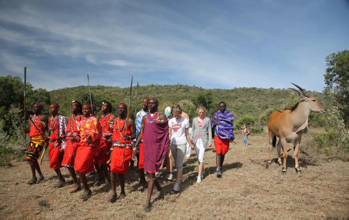 Maasai men in red shukas walking with visitors across open grassland