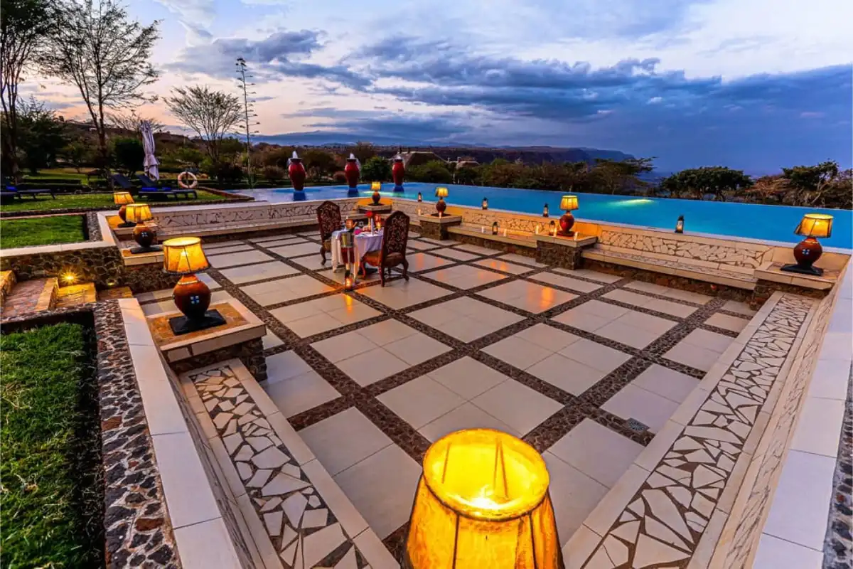 A lodge terrace at dusk, lanterns lit beside the pool