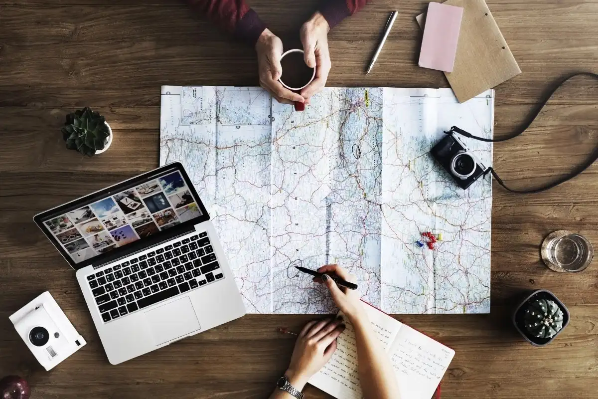 Planning a route on a paper map beside a laptop and a camera