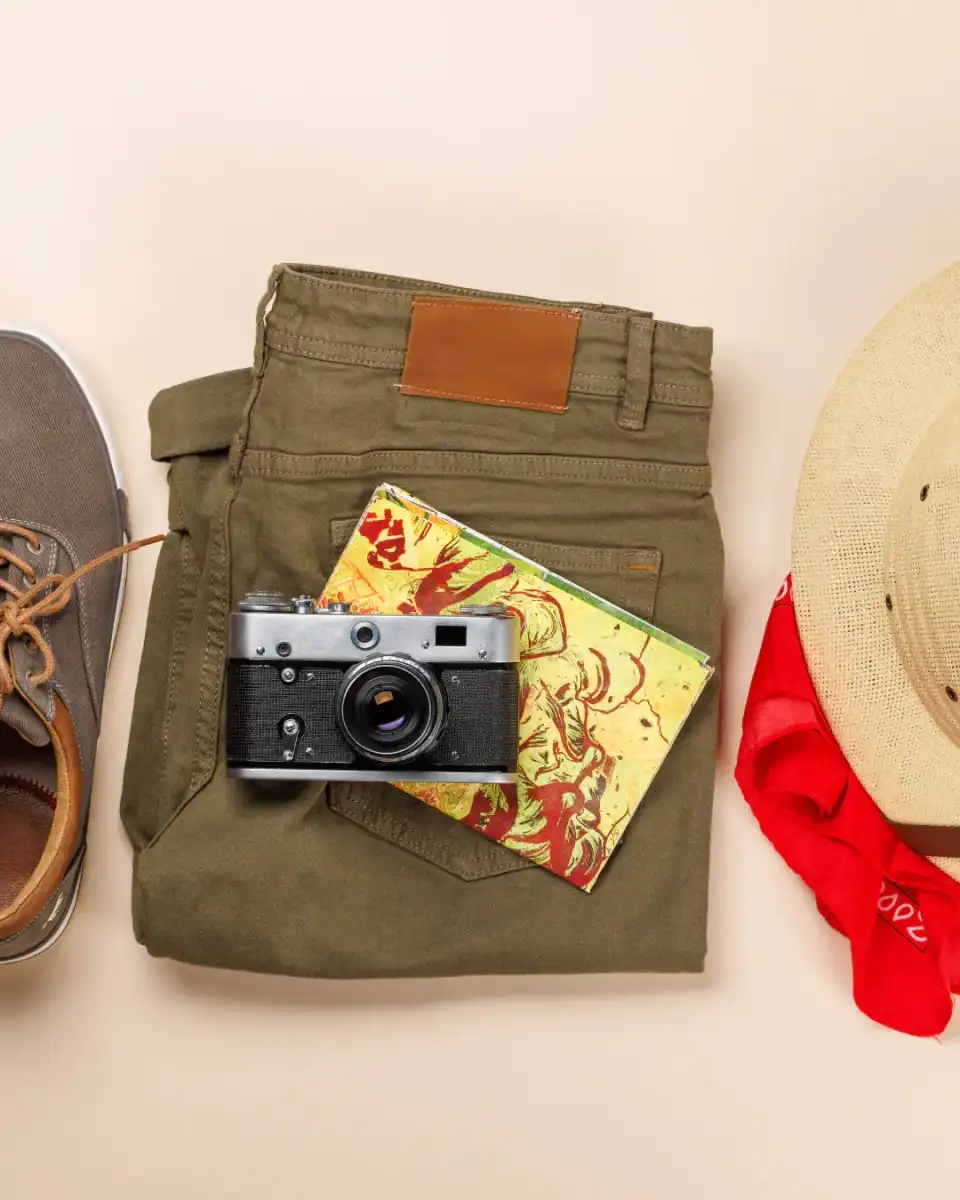 A flat-lay of trekking trousers, boots, a camera and a hat