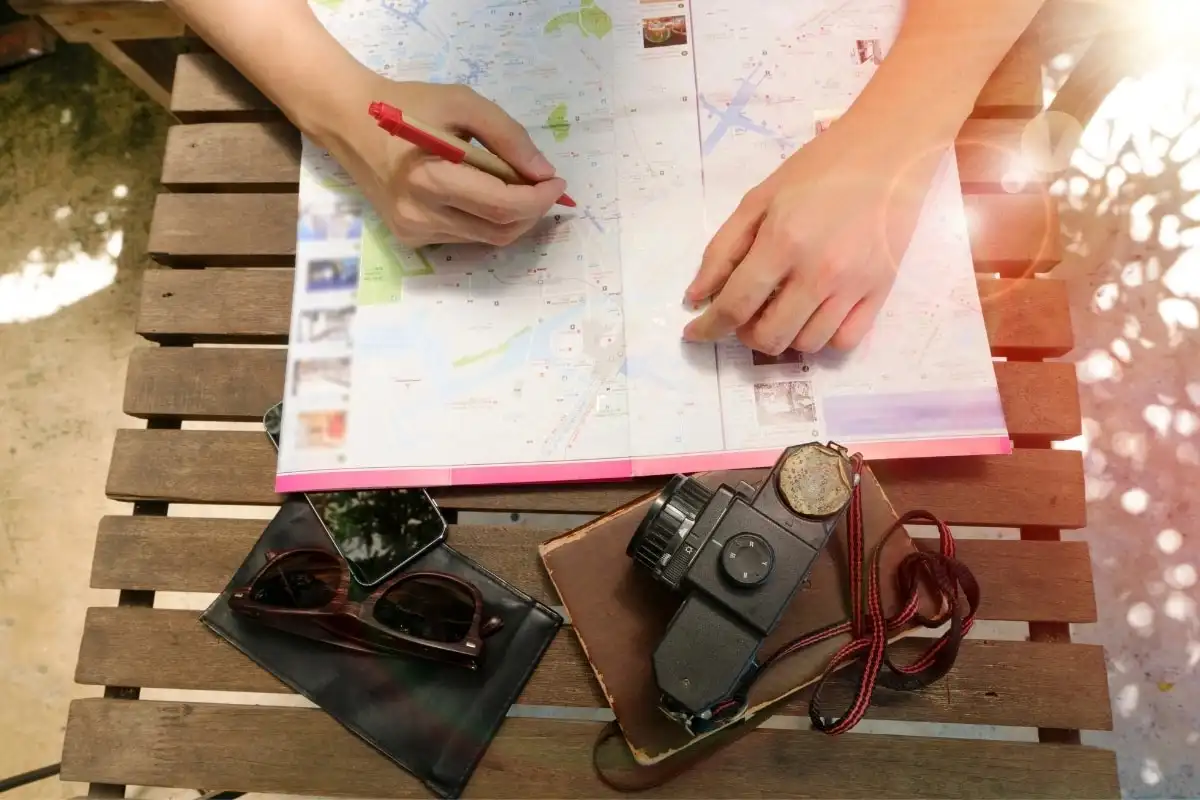 Writing in a notebook over a map, with a camera and sunglasses alongside