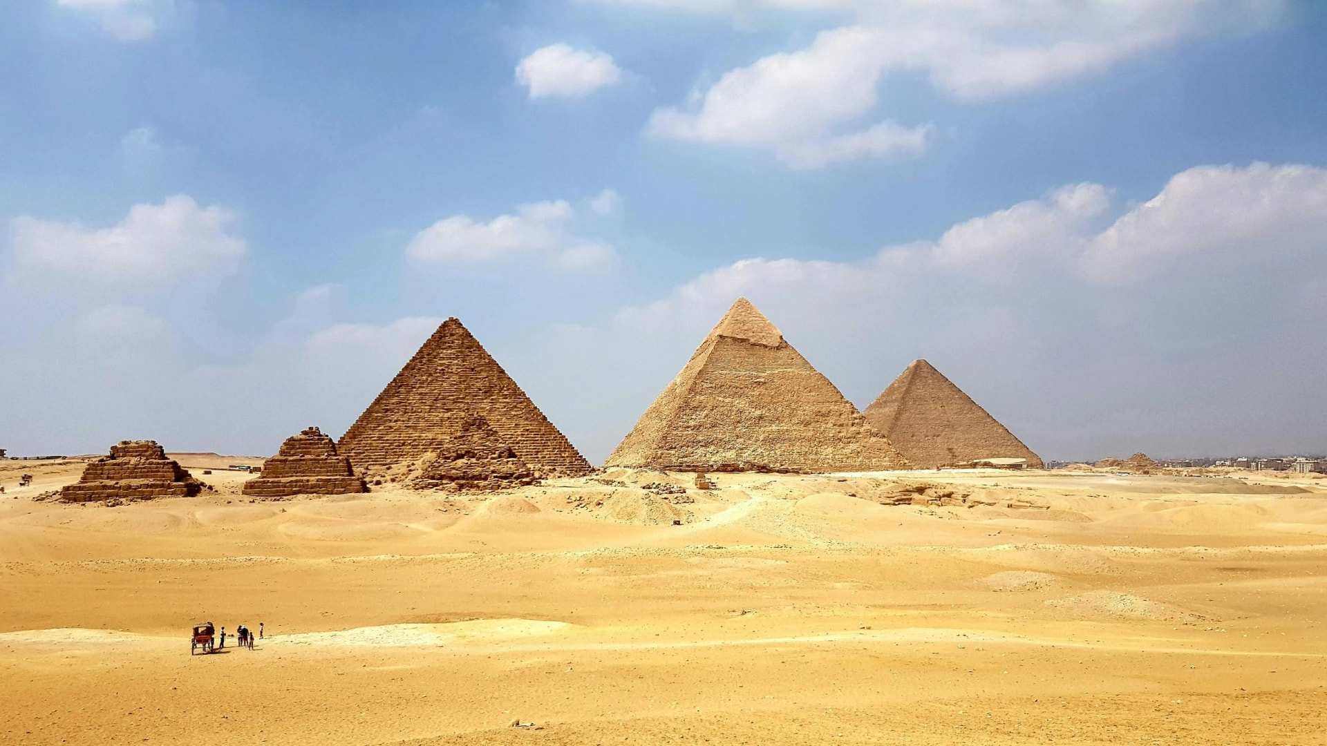 The pyramids of Giza on the open desert, a carriage and a few visitors small in the foreground