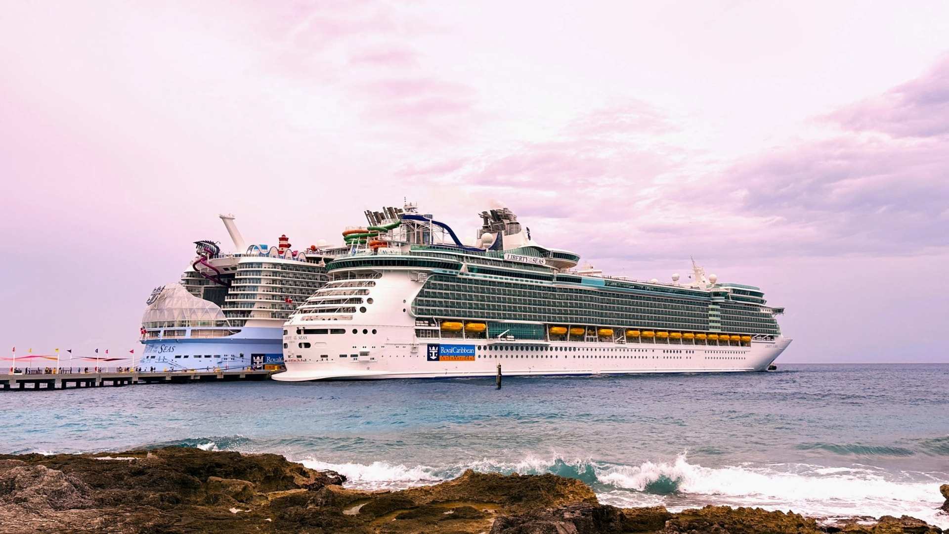 Two cruise ships moored beyond a rocky shore at dusk