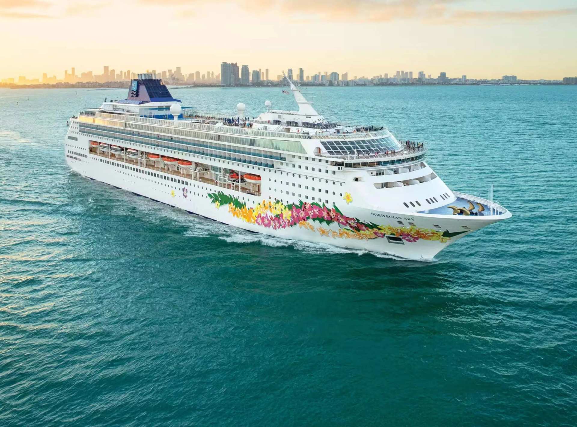 A cruise ship at sea with a city skyline behind it
