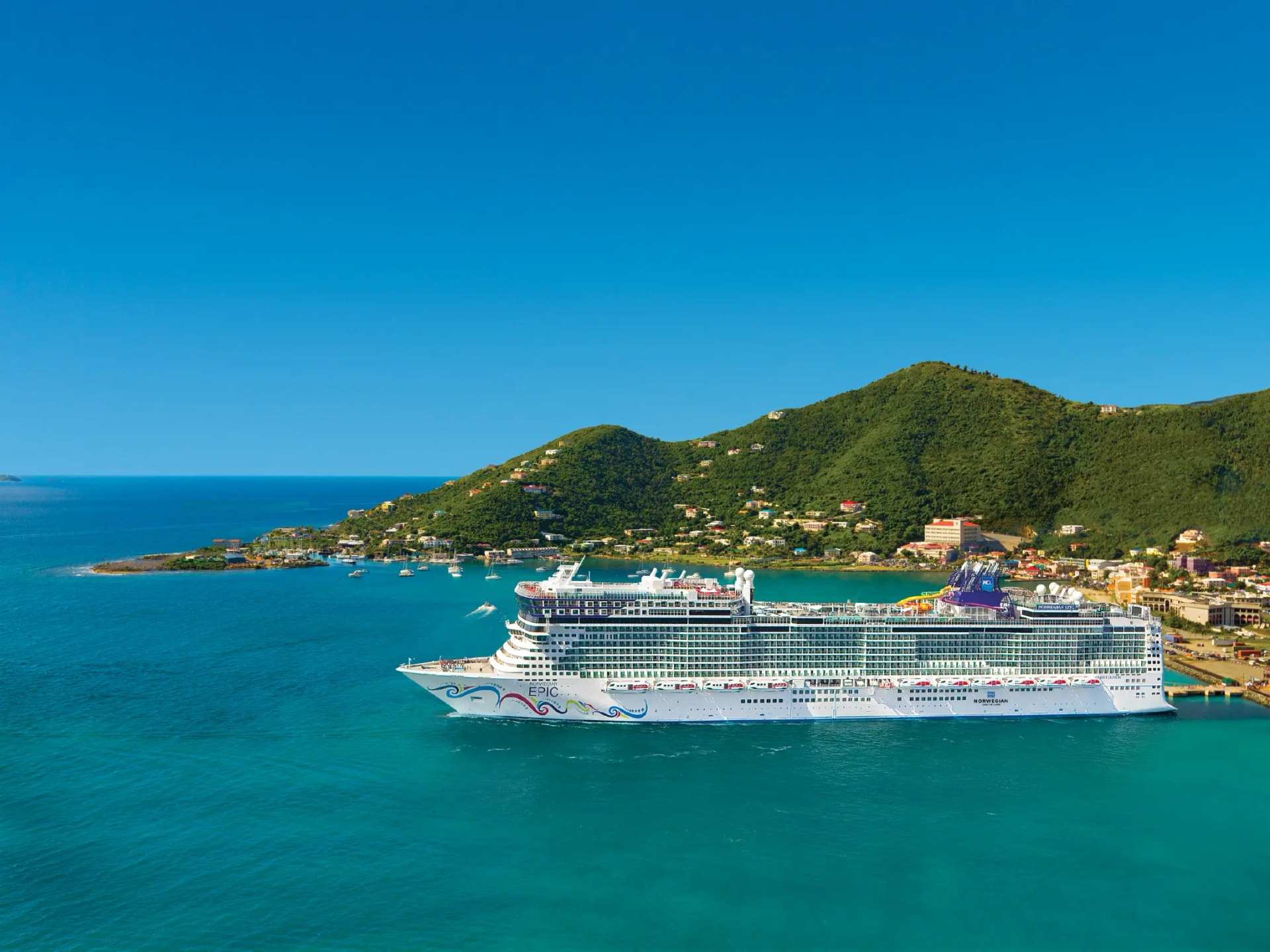 A cruise ship anchored off a green headland in turquoise water