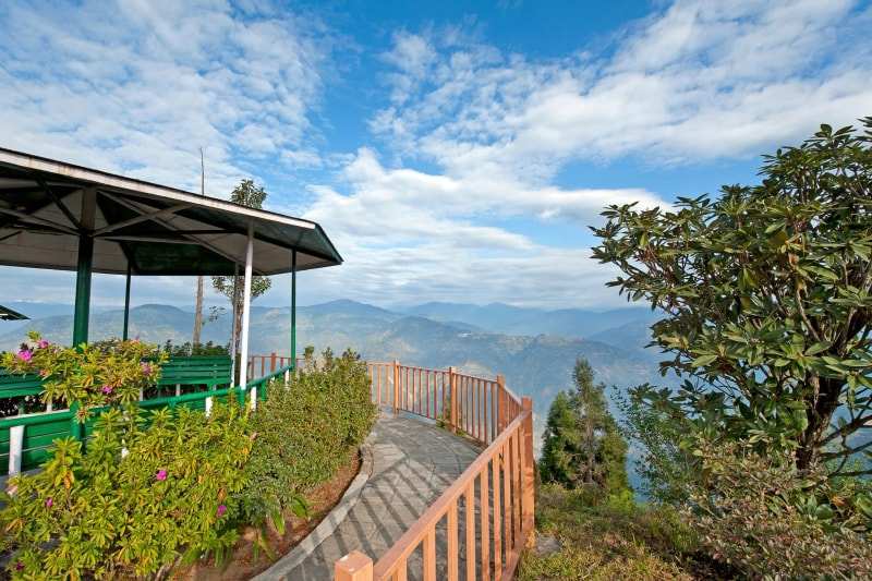 A gazebo and railed path at a hilltop viewpoint in Kalimpong, blue foothills fading into haze beyond