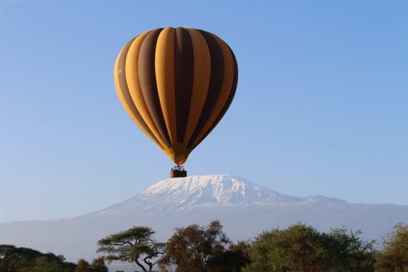 A hot-air balloon with a basket of passengers floating in front of the snows of Kilimanjaro