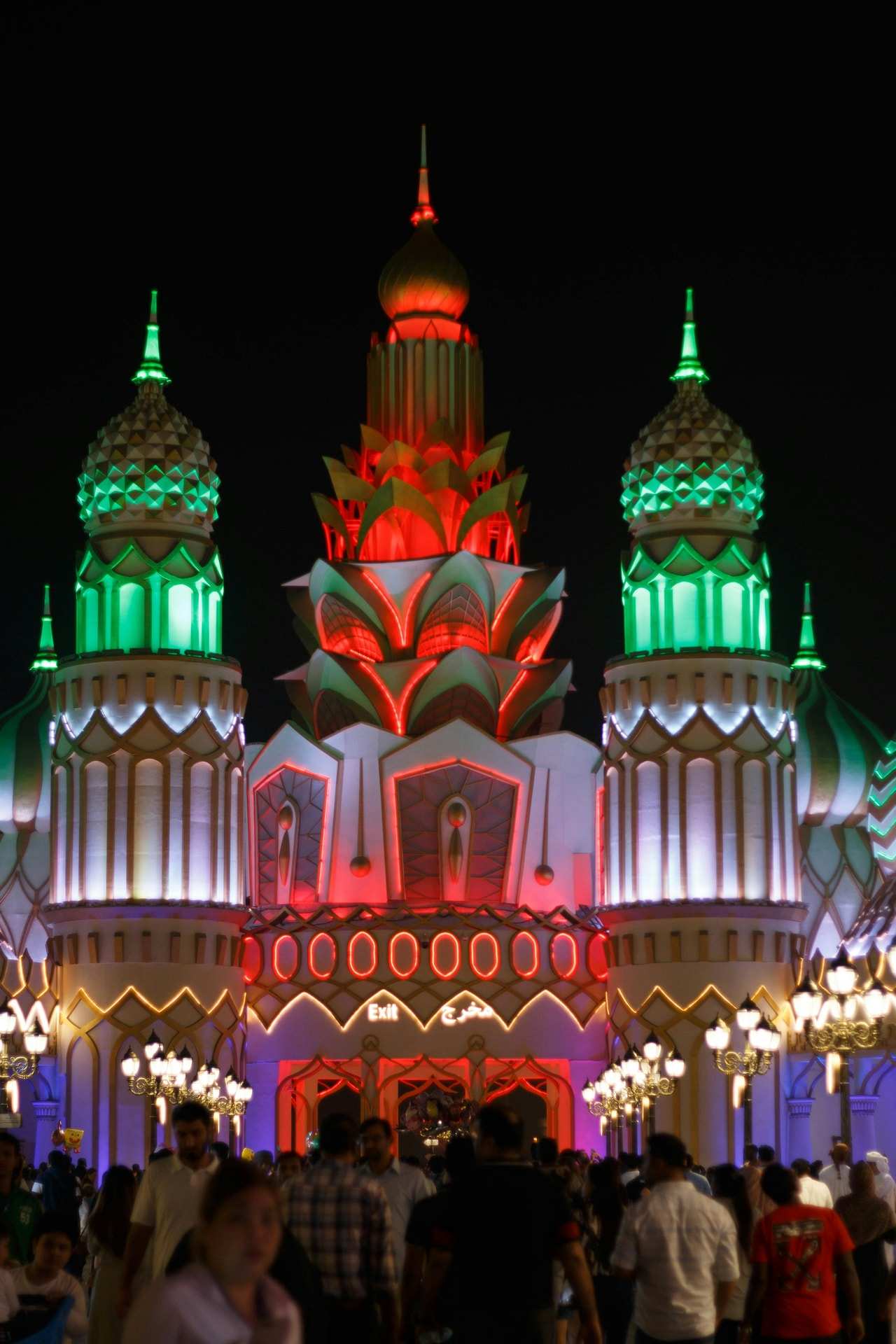 A pavilion at Global Village in Dubai lit green, red and white at night, with visitors in front of it