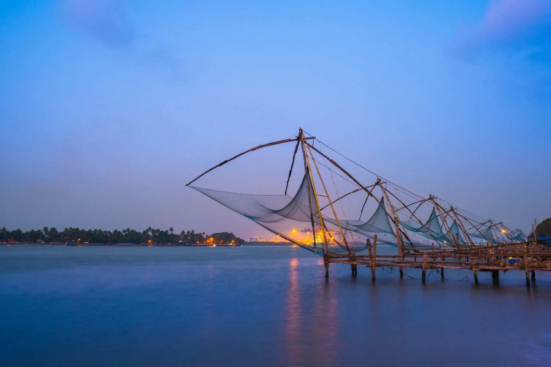Chinese fishing nets on their timber frames at Kochi, lights coming on across the water at dusk