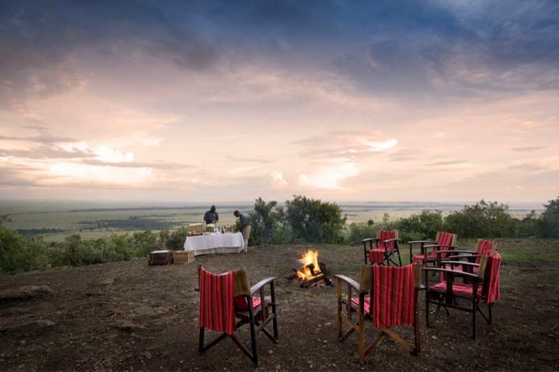 A firepit and canvas chairs set out on a bluff at sunset, the plains falling away behind