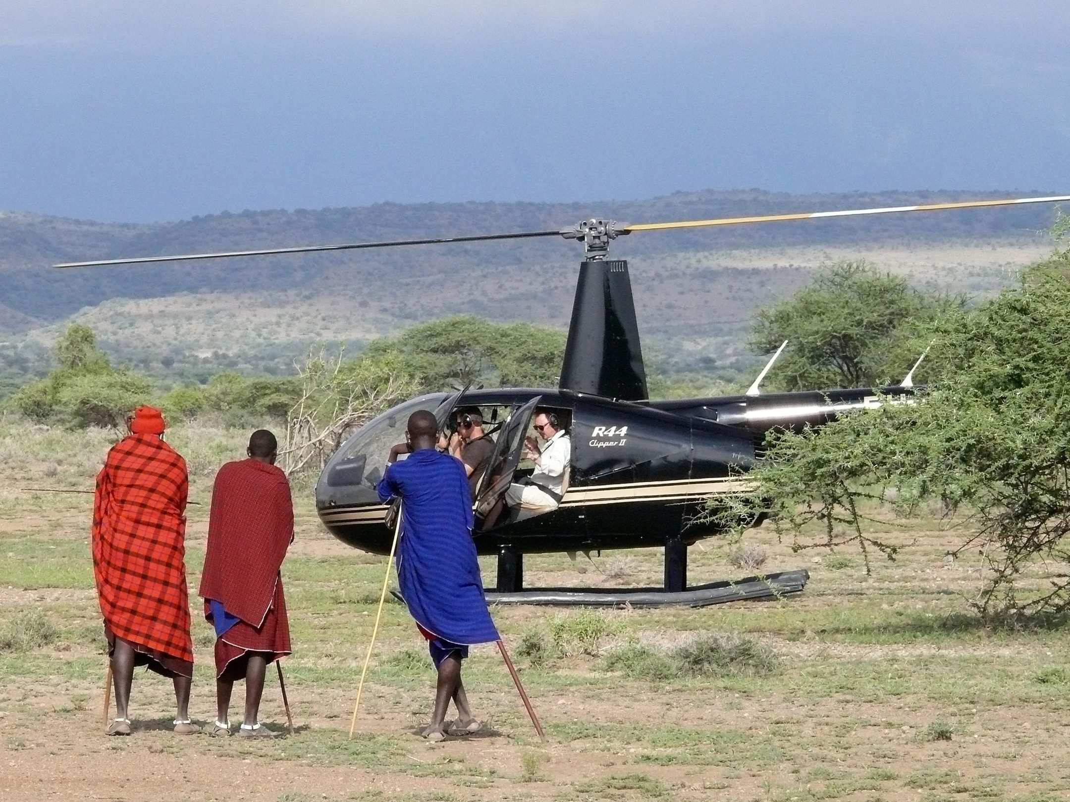 Maasai in red shukas beside a helicopter landed on the plain