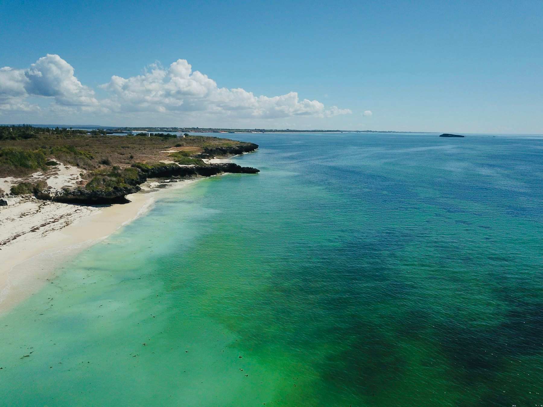White sand and turquoise shallows along a coral-rock coastline seen from the air