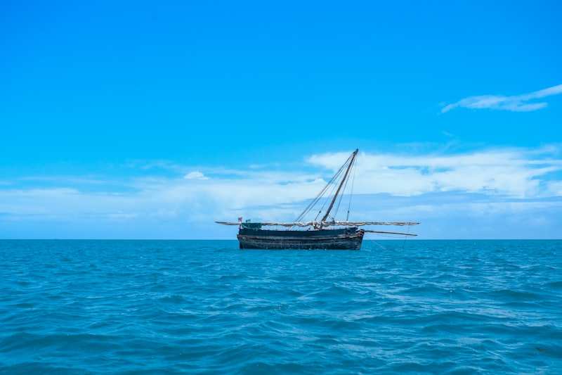 A wooden dhow lying at anchor on open blue water under a bright sky