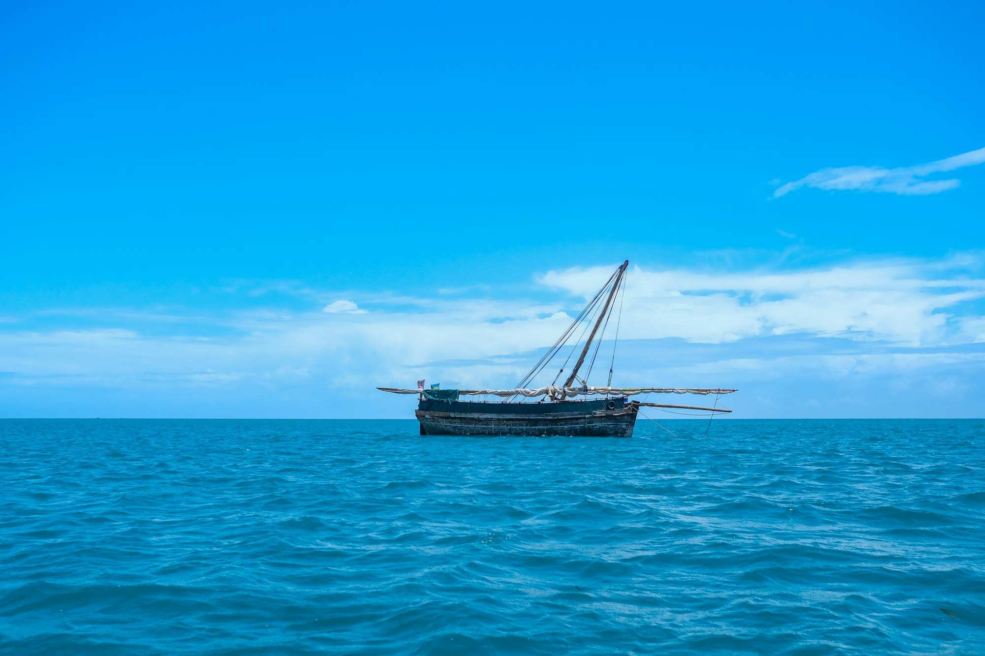 A wooden dhow lying at anchor on open blue water under a bright sky