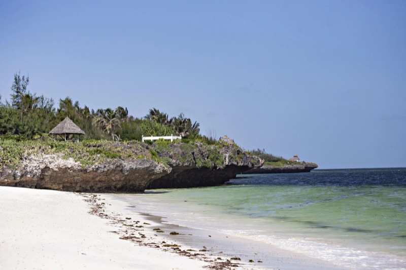 White sand running along a low coral cliff, a thatched banda above it and the reef beyond