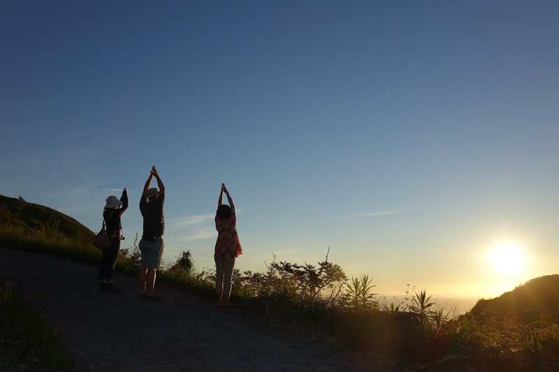 Three people stretching into a yoga pose on a hillside path as the sun drops