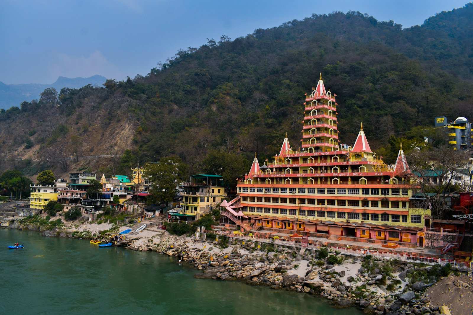 The tiered Trayambakeshwar temple rising above the Ganges at Rishikesh, rafts drawn up on the bank