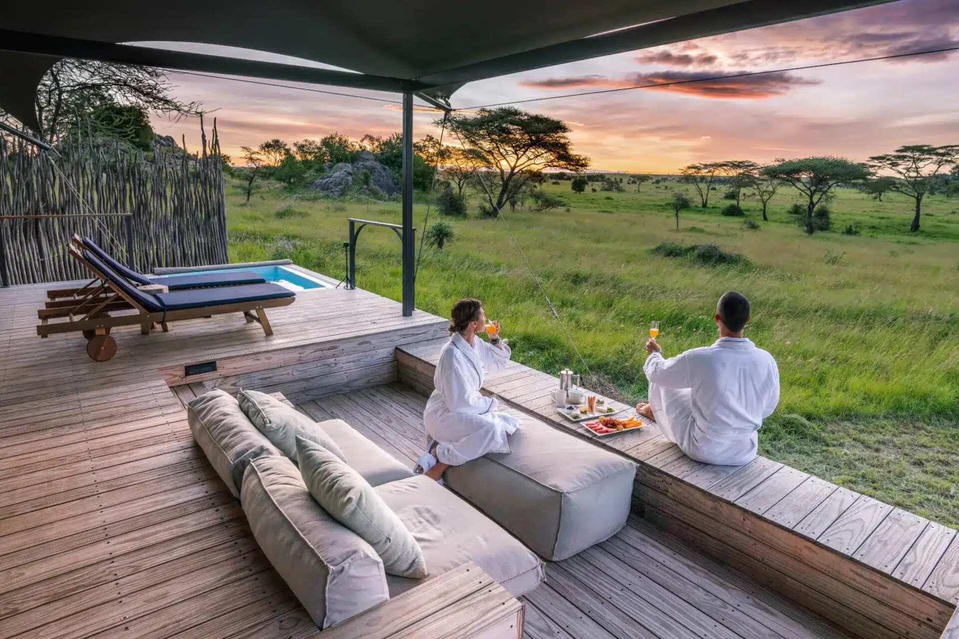 A couple in robes on a private deck at sunrise, looking out over open plains
