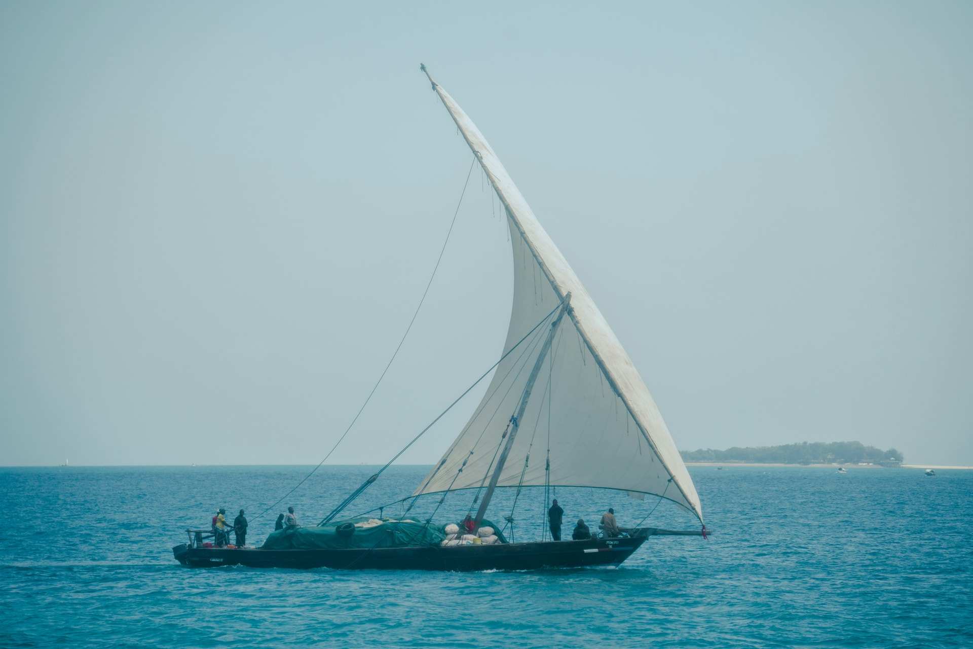 A dhow under a single white sail crosses the sea off Zanzibar, with a low island on the horizon