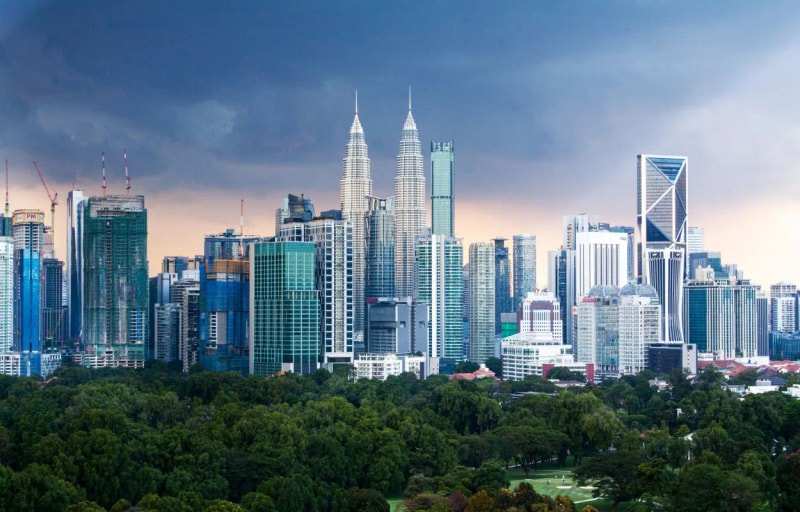 The Kuala Lumpur skyline under a stormy sky, the Petronas Twin Towers at its centre and parkland in front