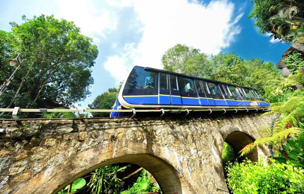 The blue Penang Hill funicular train crossing a stone-arched viaduct among tropical trees