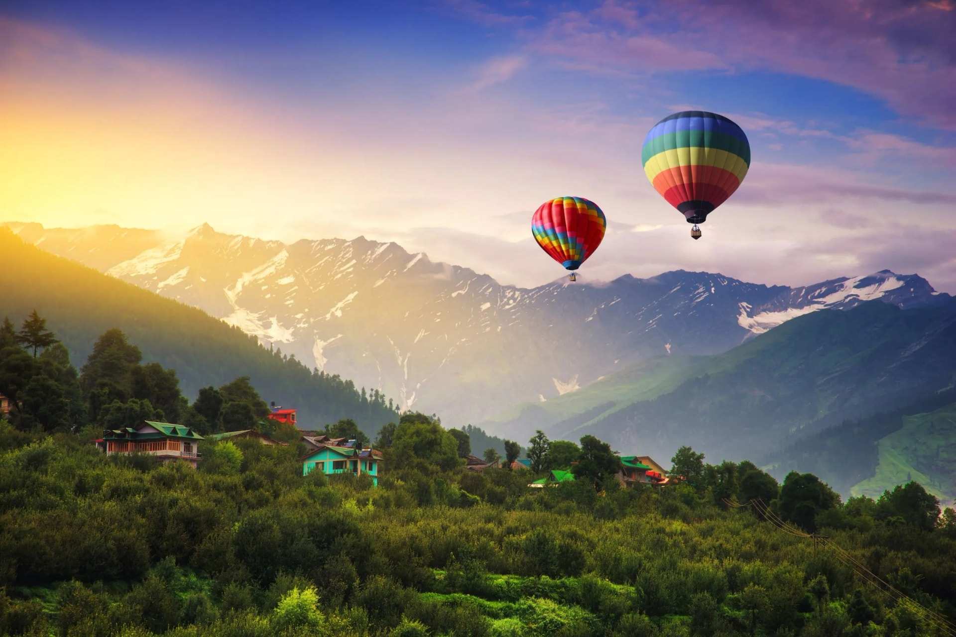 Two hot-air balloons over a green valley below snow-capped peaks at Manali