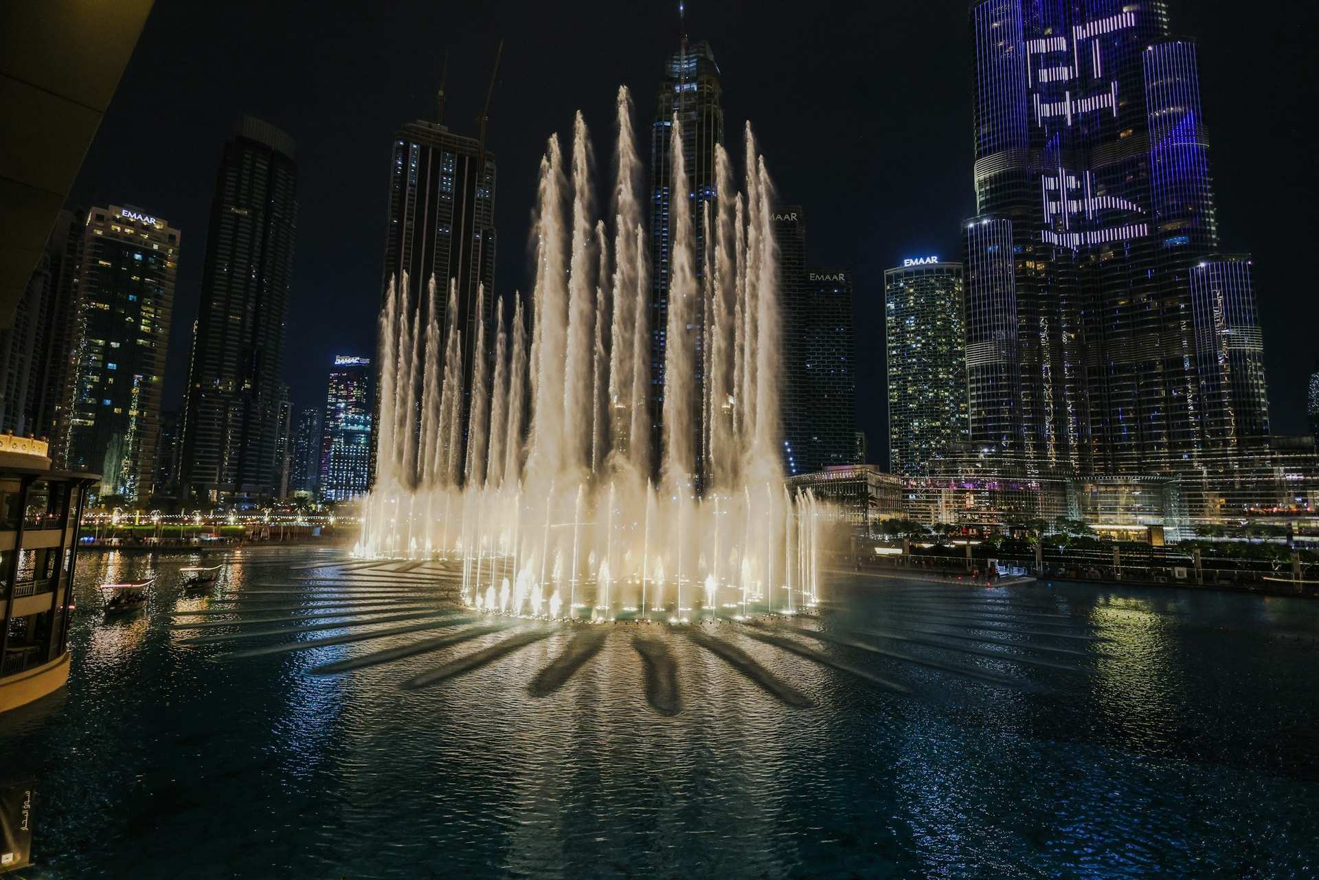 Fountain jets lit up at night on the lake beside Dubai Mall, with the Downtown towers behind