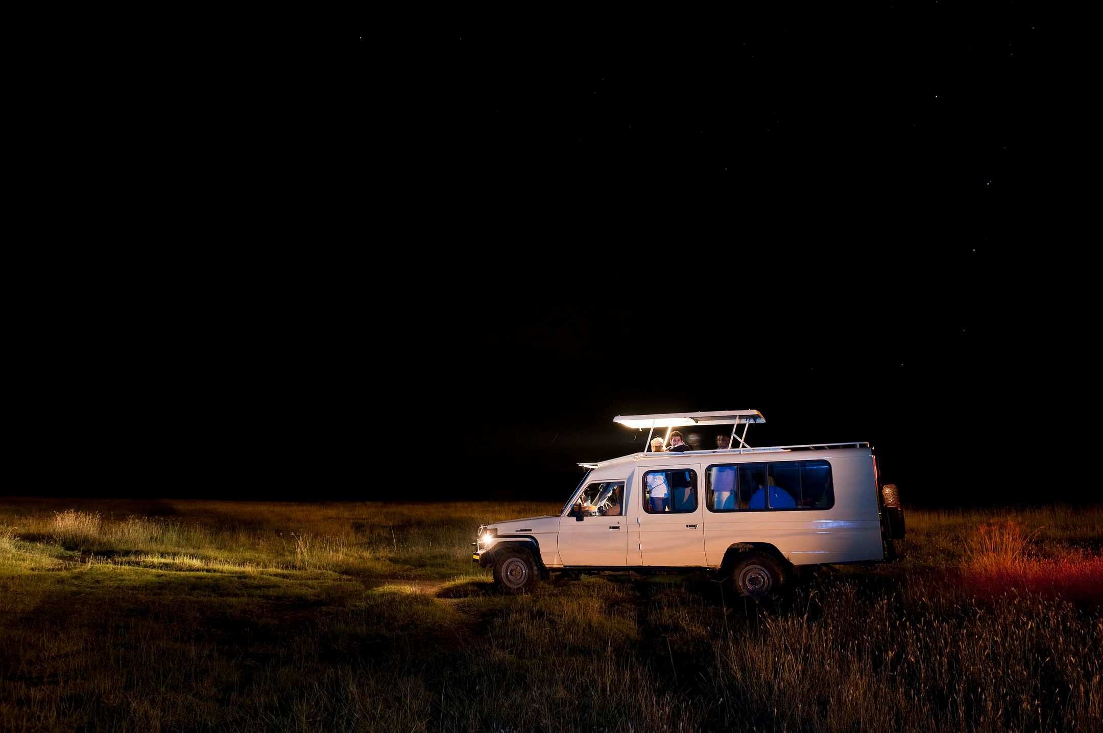 A safari vehicle picked out by a spotlight in the dark of the bush at night