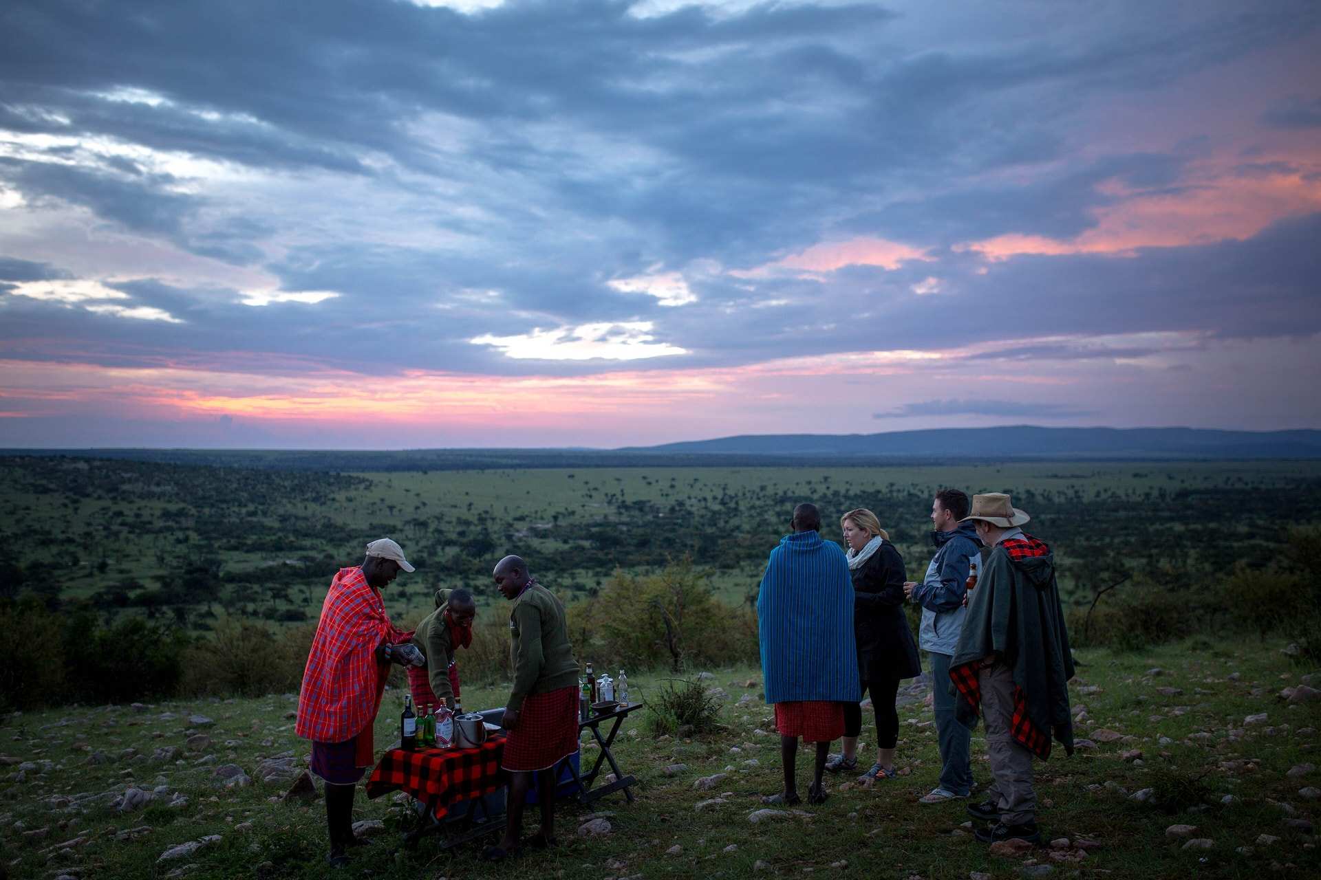 Guests and their Maasai guides gathered for sundowners on a rise above the Ol Kinyei Conservancy, the sky turning pink over the Mara