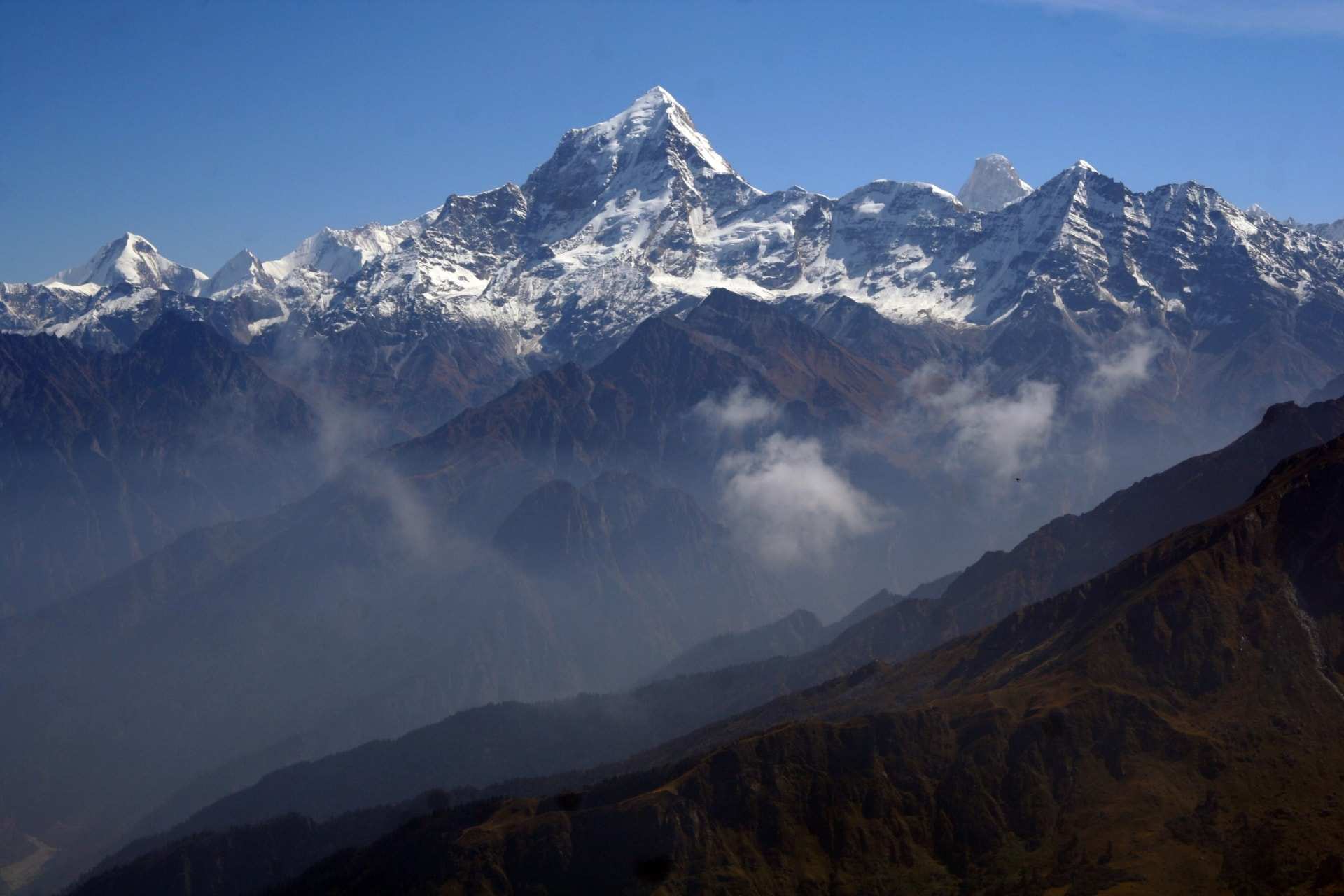 Snow-covered Himalayan peaks above hazy brown ridges, cloud drifting in the valleys below