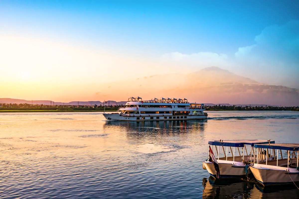 A Nile cruise boat on the river at sunset, two small launches moored in the foreground