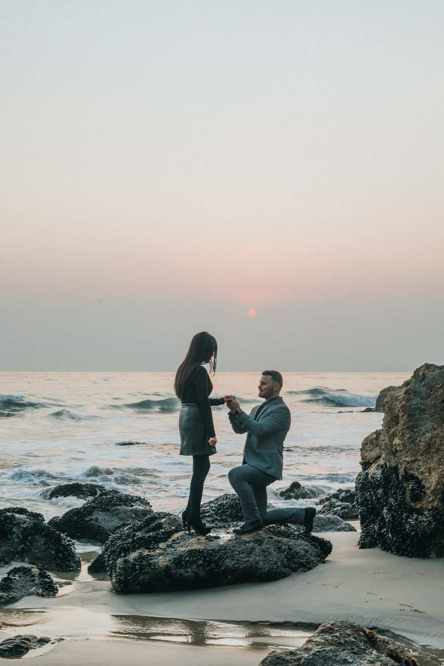 A man on one knee at the water's edge as the sun drops behind the sea