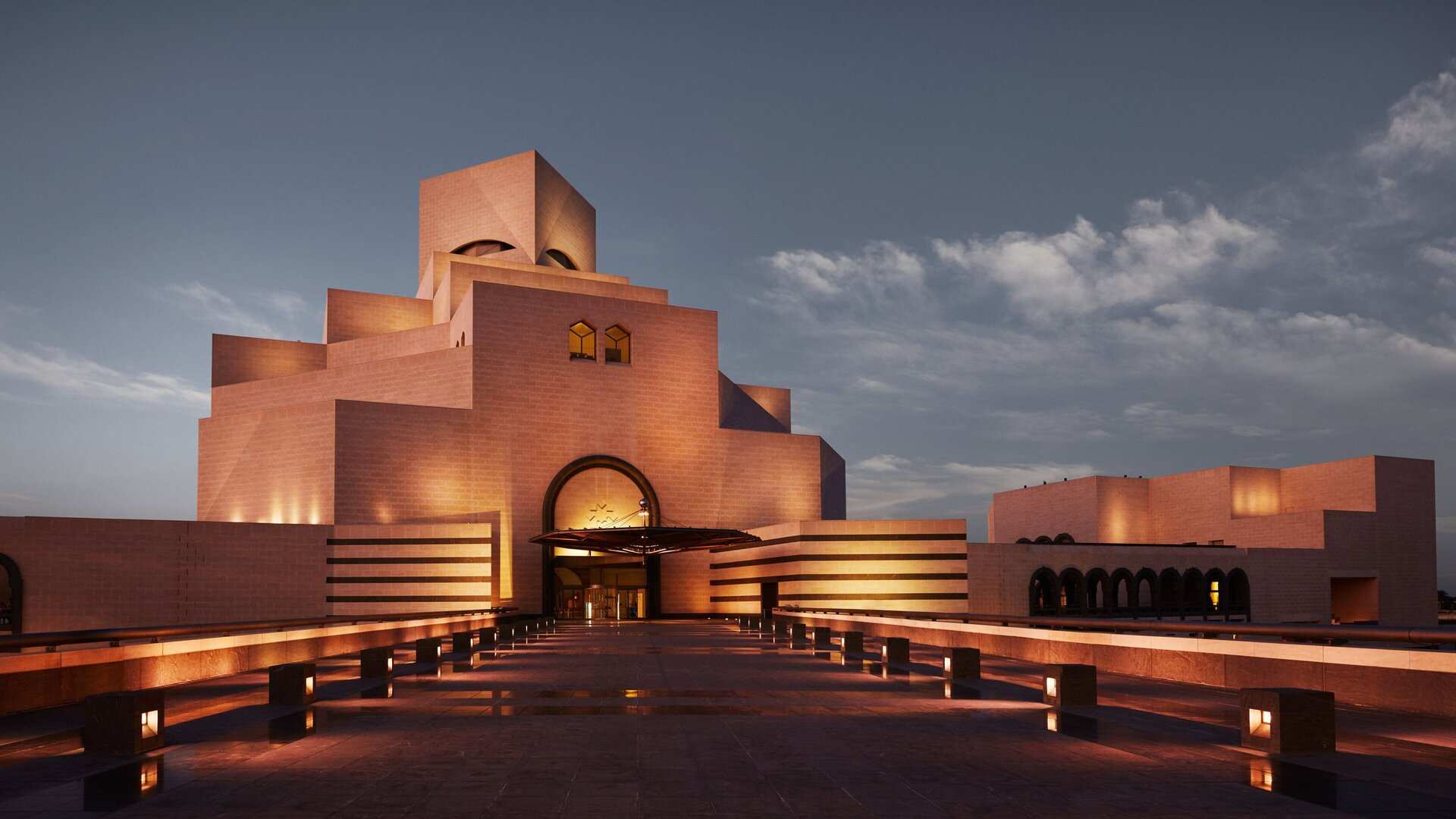 The Museum of Islamic Art in Doha, its stacked limestone blocks floodlit at dusk above the entrance plaza