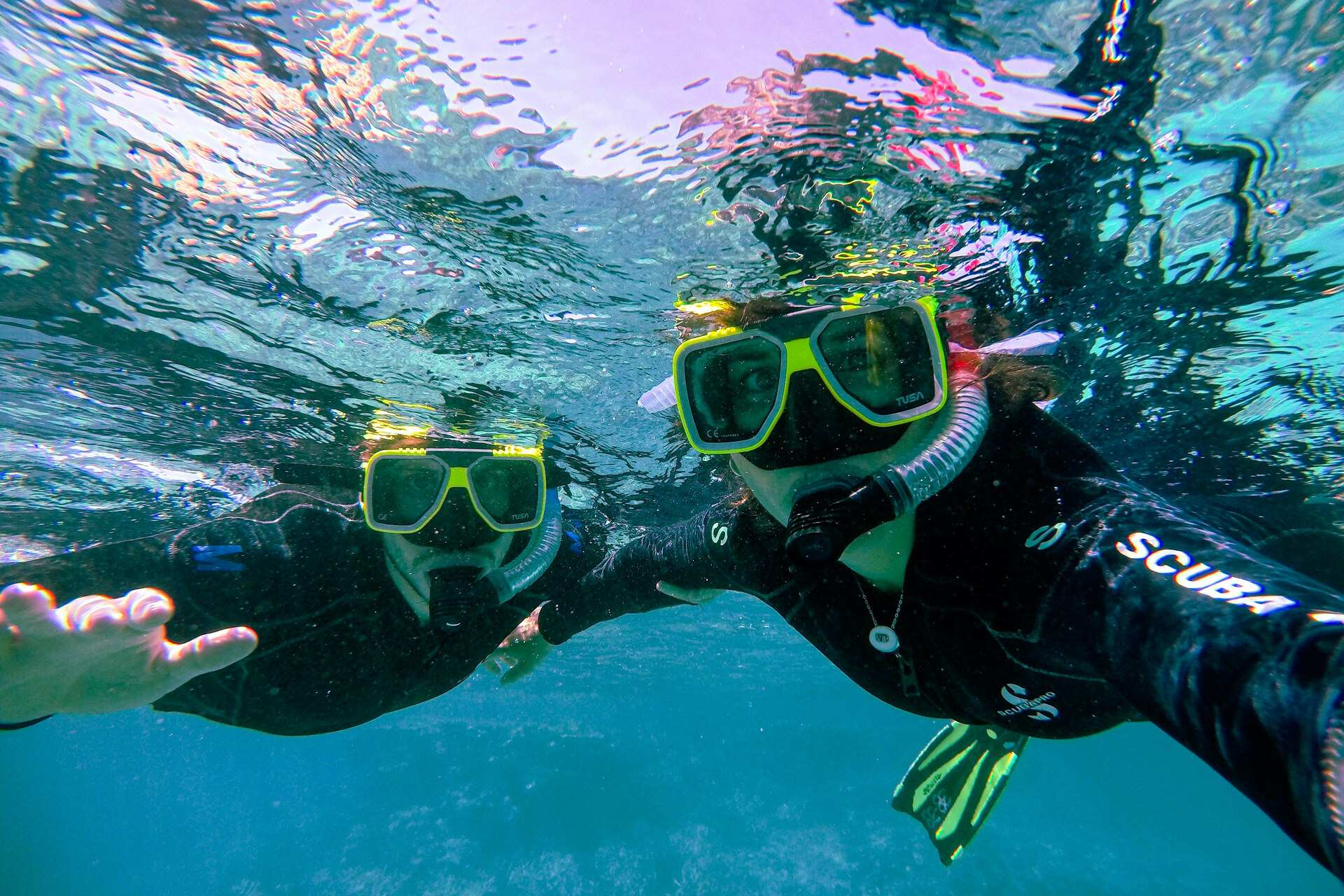 Two snorkellers in wetsuits and masks just under the surface in clear turquoise water