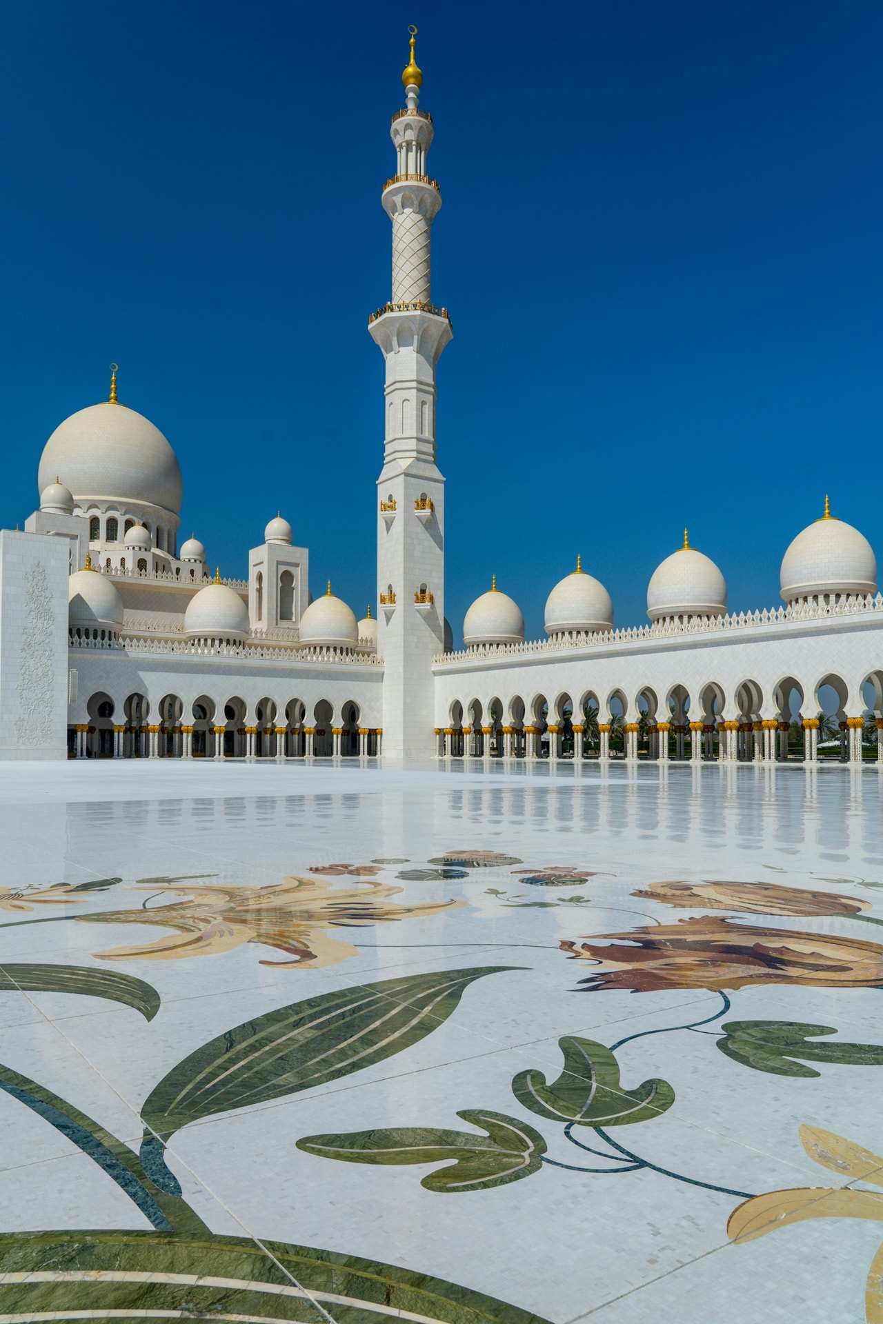 The white domes and a minaret of the Sheikh Zayed Grand Mosque in Abu Dhabi, above its flower-inlaid marble courtyard