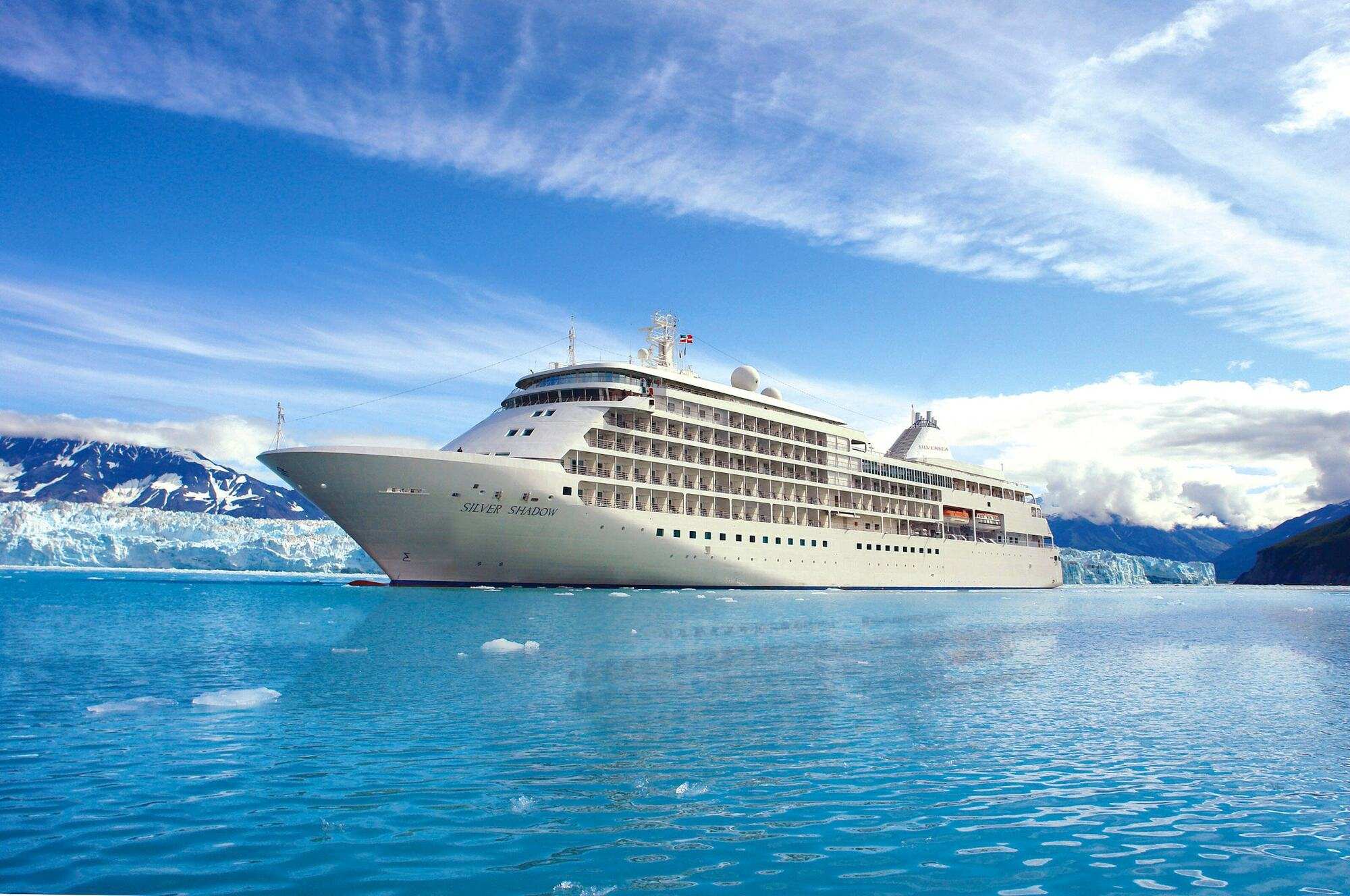 Silver Shadow at anchor on turquoise water in front of a glacier face, snow-covered mountains behind