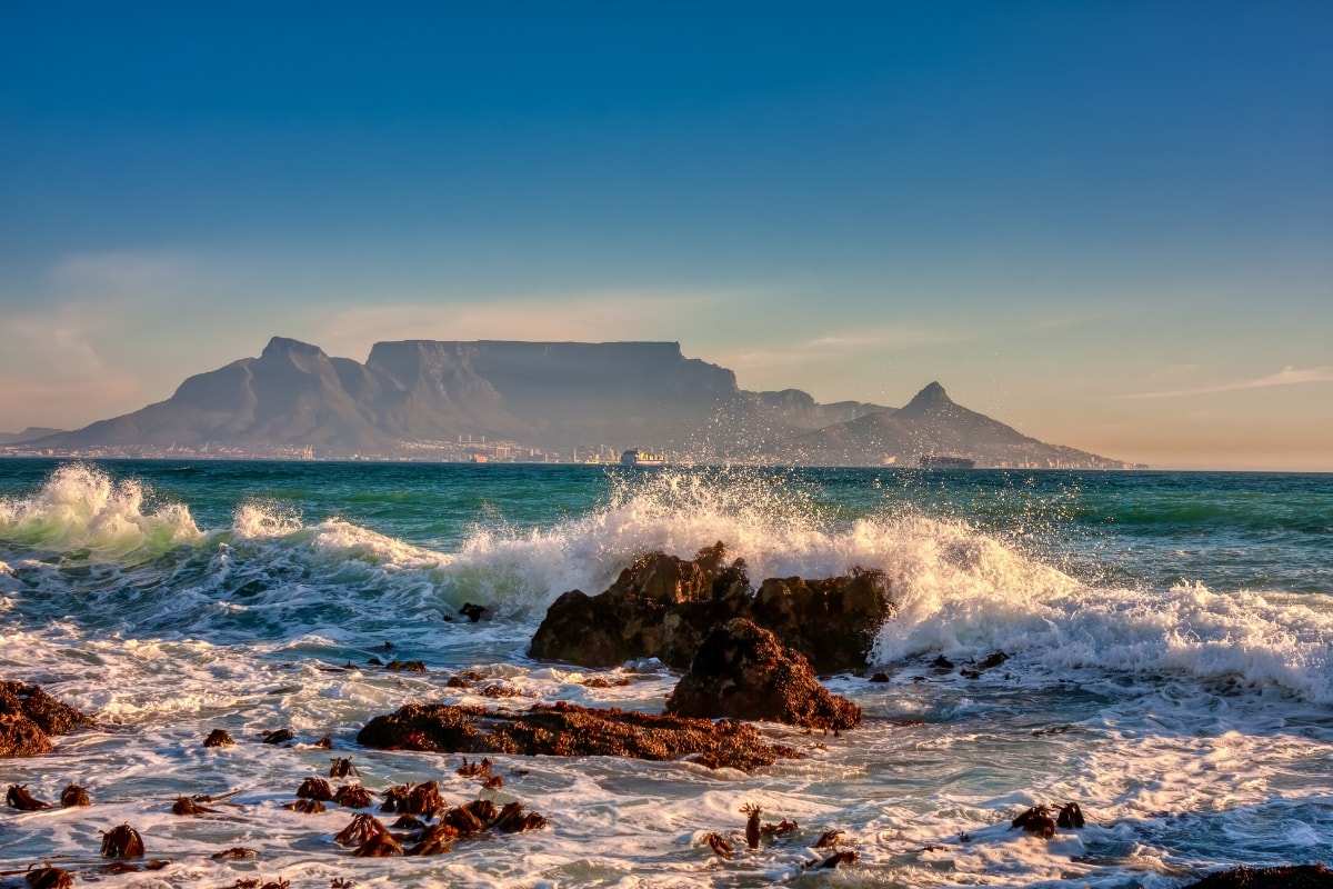 Table Mountain across Table Bay, waves breaking over dark rocks in the foreground